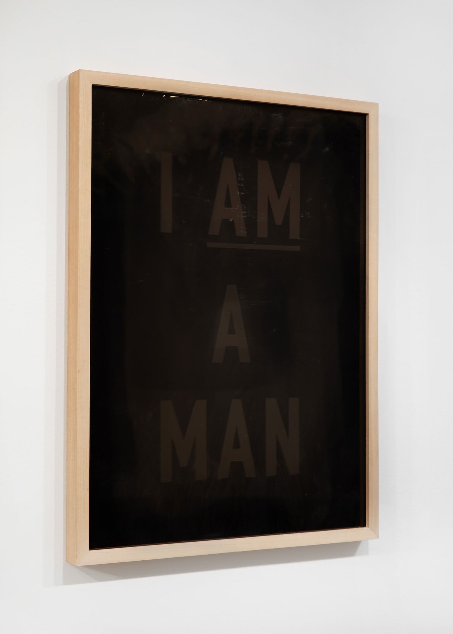 A framed print of the text "I AM A MAN" in the style of the famous protest sign from The 1968 Memphis Sanitation Workers’ Strike, printed black on black